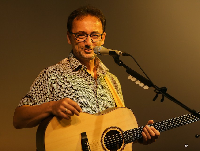 Lutz Scheufler lächelnd mit Gitarre am Mikrofon