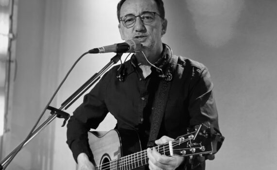 s/w-Foto Lutz Scheufler mit Gitarre während einer Veranstaltung